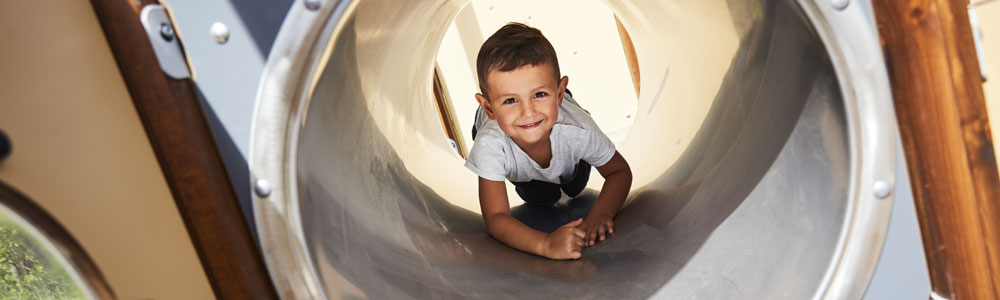 Ragazzo che striscia attraverso un tunnel in un parco giochi inclusivo